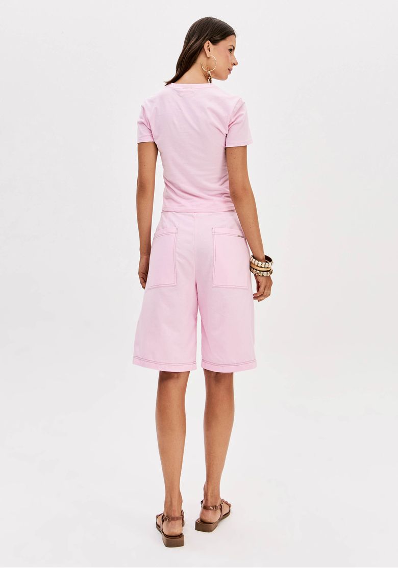 Modelo vestindo bermuda rosa com camiseta estampada e sandálias, vista traseira.