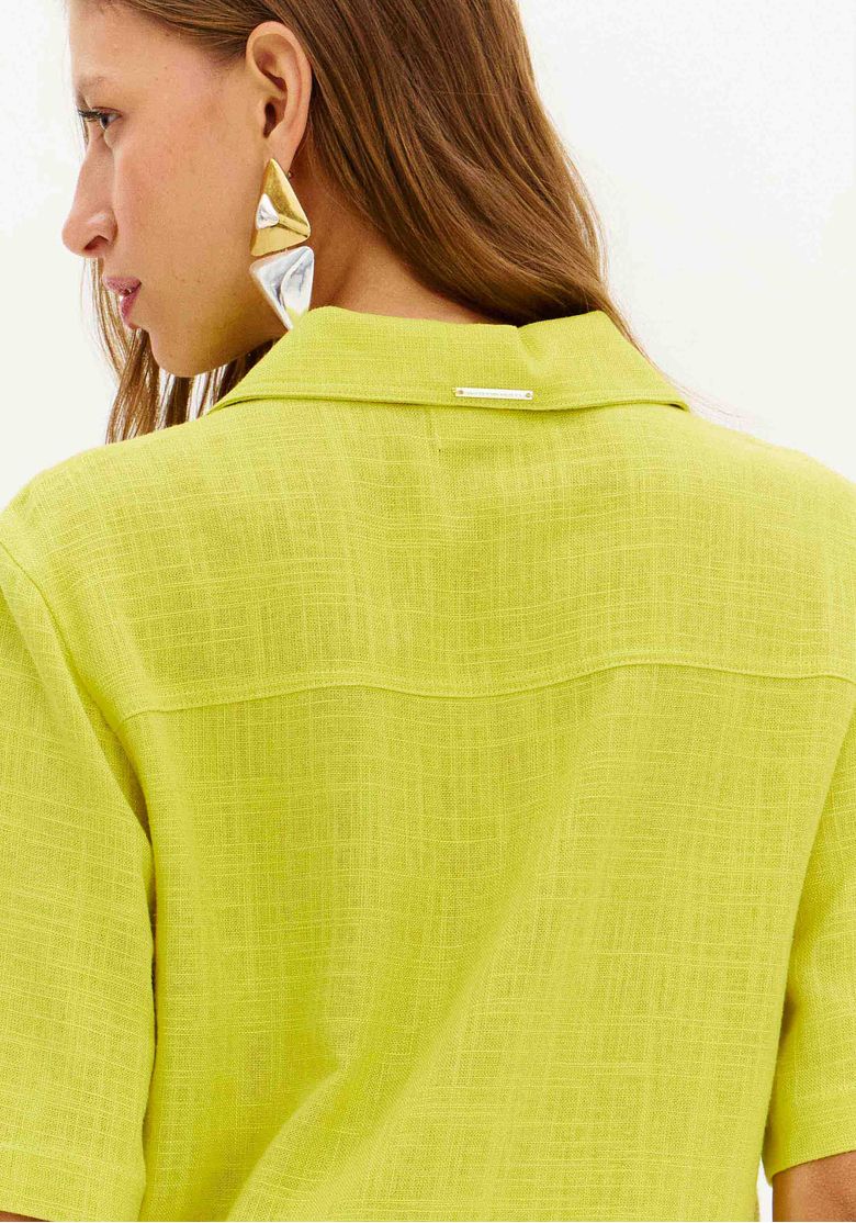 Detalhe lateral da camisa curta em linho amarelo, mostrando o tecido texturizado.