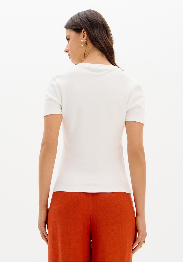Close-up do torso da camiseta baby look branca destacando o bordado discreto no peito e a textura da malha pesada 100% algodão