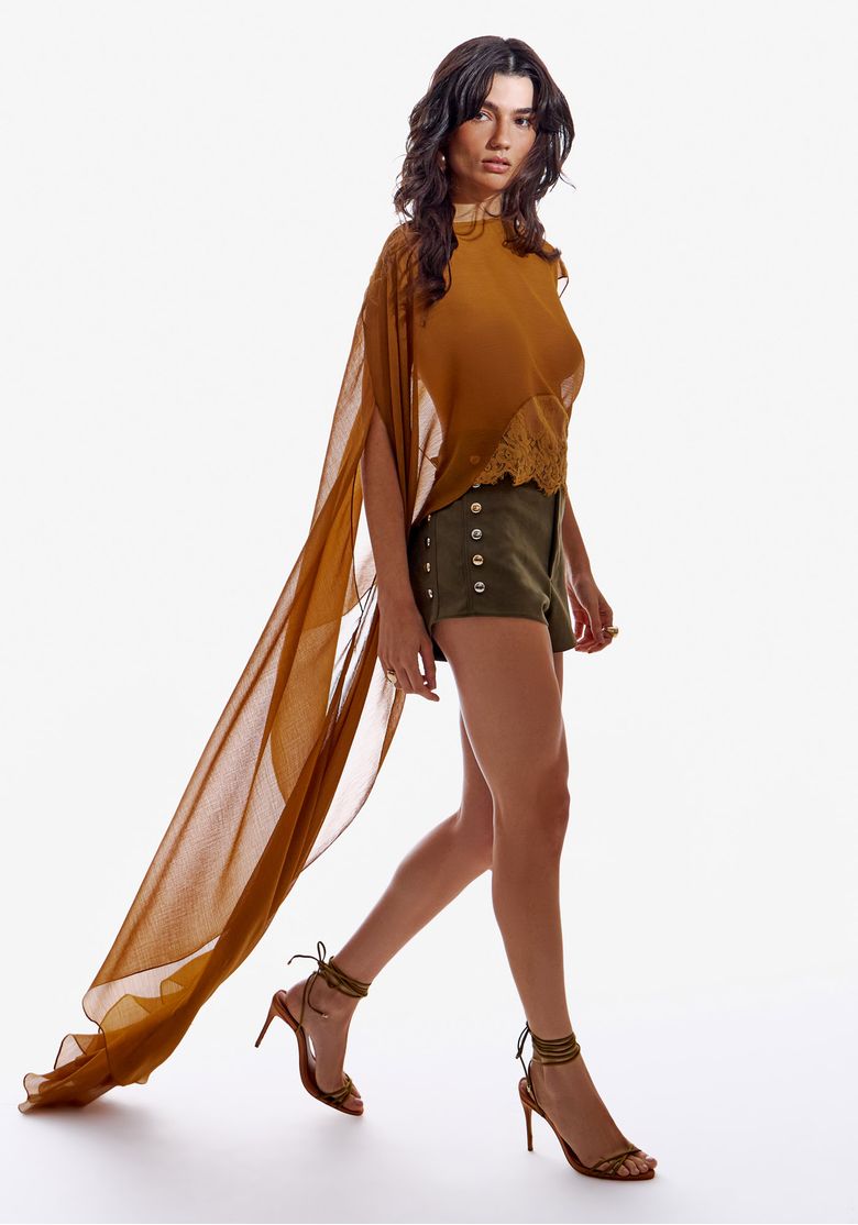 Blusa assimétrica com detalhe de renda vista de frente, combinada com shorts e sandálias.