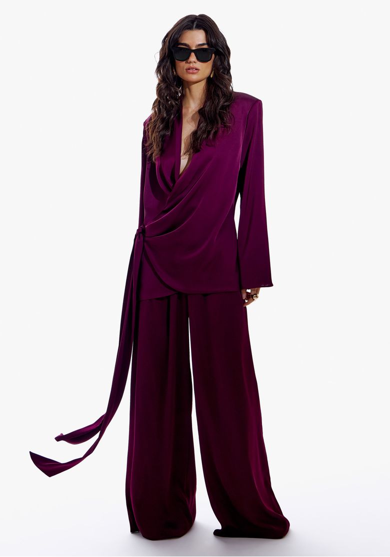 Modelo vestindo calça wide leg de cetim vinho com blazer combinando, em pose frontal.