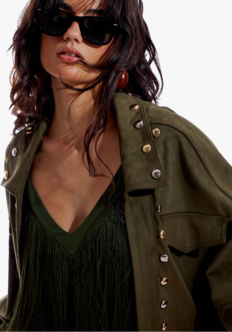 Visão de corpo inteiro da jaqueta bomber suede verde com barra ajustável, saia em camadas e sandálias, styling editorial.