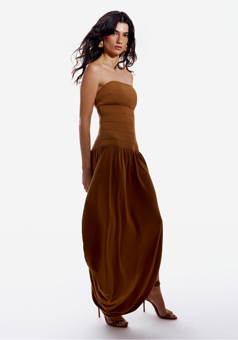 Modelo em estúdio usando vestido super midi sem alça caramelo, vista frontal mostrando corpo estruturado e saia drapeada com barra assimétrica