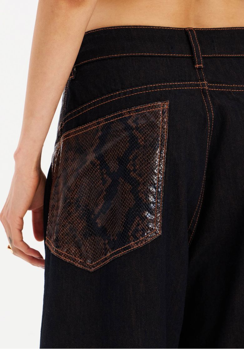 Detalhe do bolso traseiro com revestimento em estampa snake, textura levemente brilhante e costura contrastante na calça preta