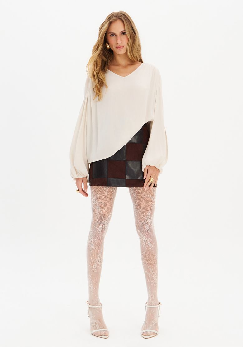 Modelo usando blusa ampla de crepe branco com saia curta e sandálias.