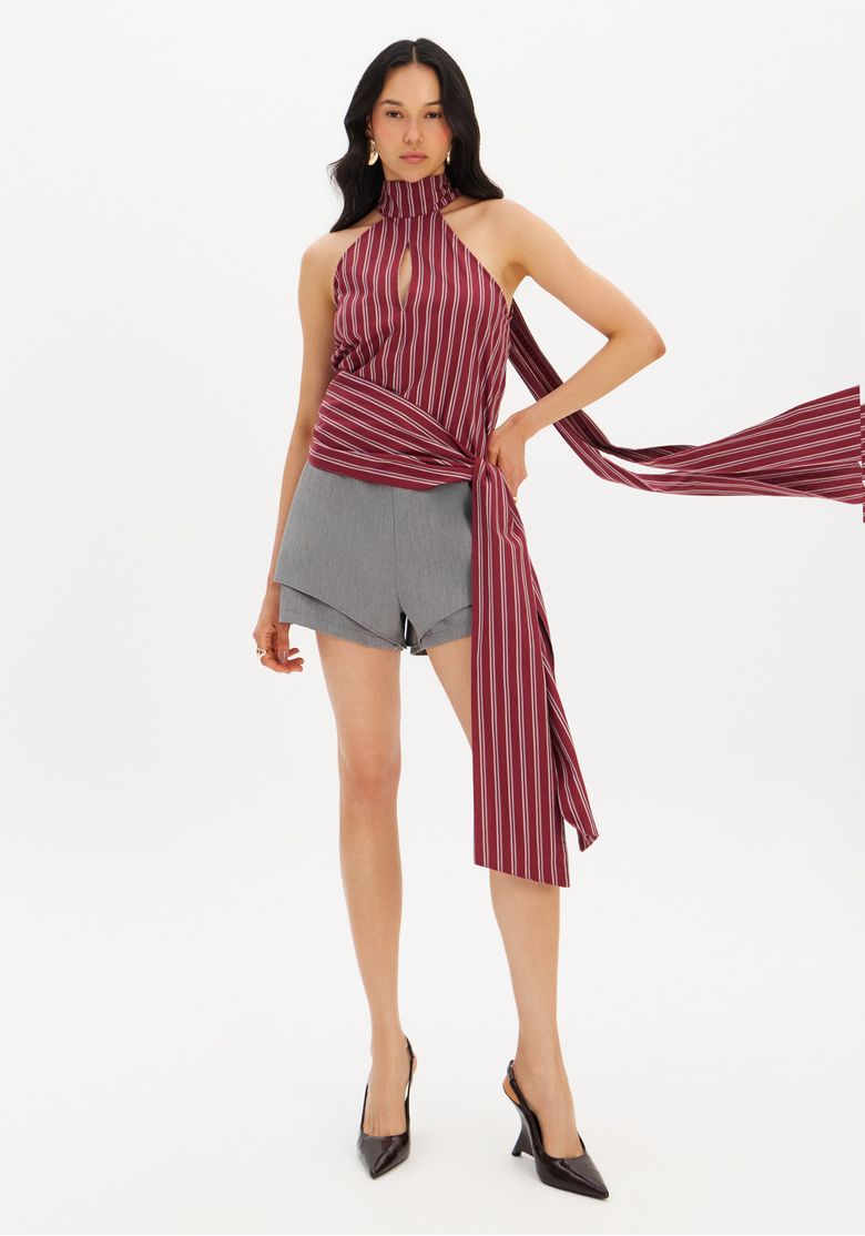 Modelo-em-pe-usando-blusa-gola-alta-listrada-vermelha-vista-frontal-com-amarracao-lateral-e-comprimento-medio