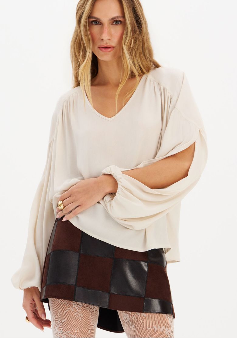 Detalhe das mangas amplas com recortes da blusa de crepe branco.
