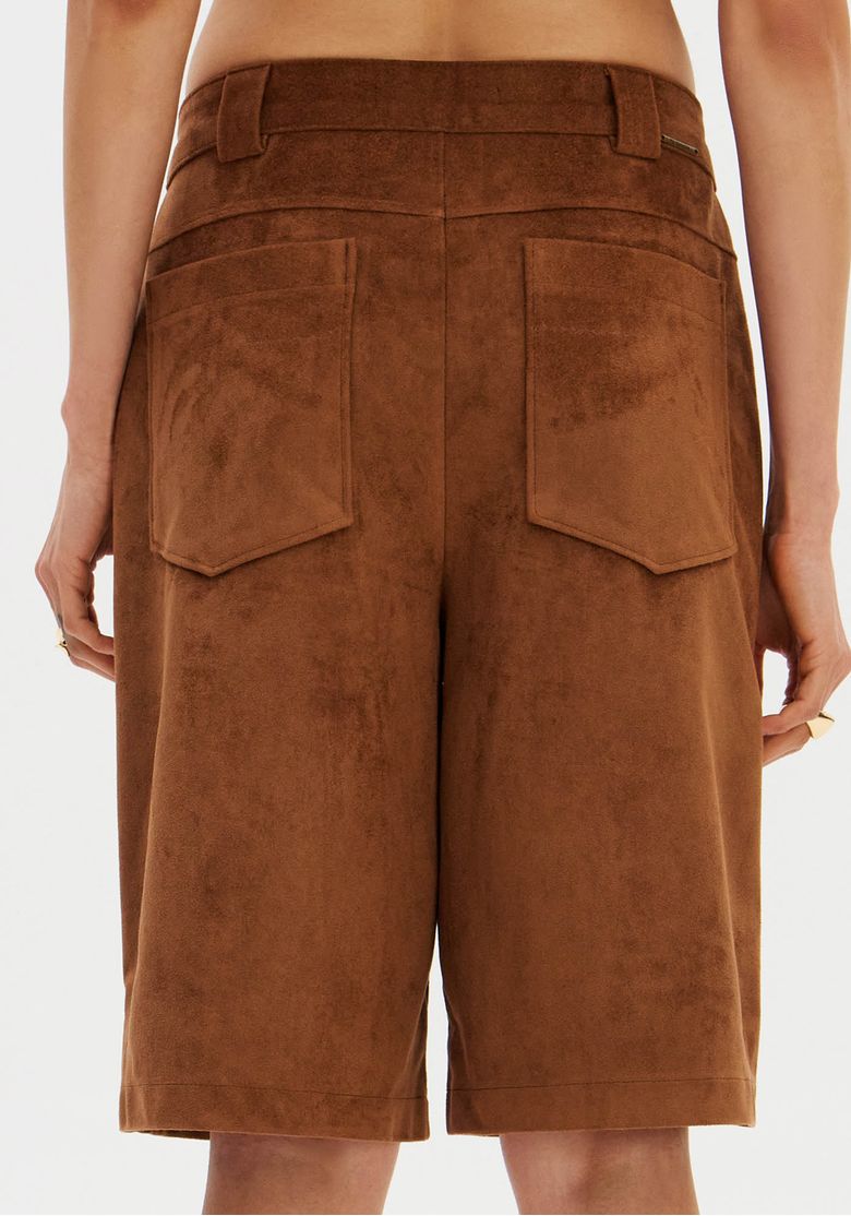 Vista-traseira-da-bermuda-suede-marrom-em-modelo-mostrando-caimento-alongado-e-bolsos-traseiros