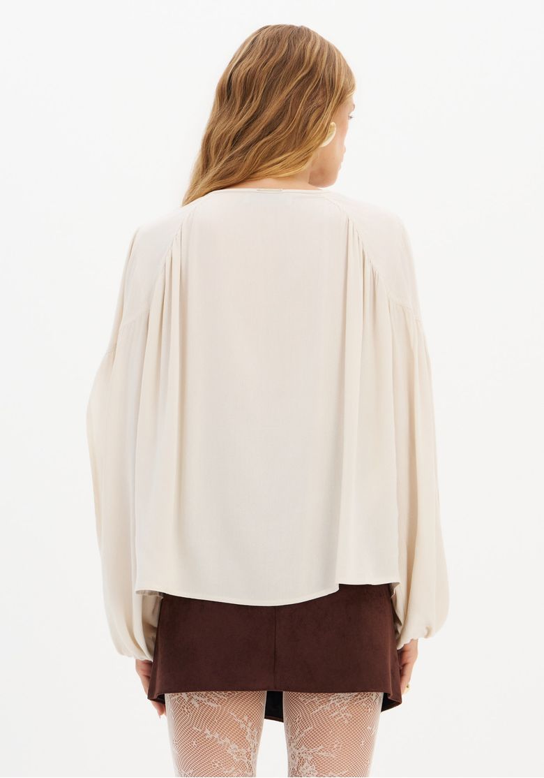 Vista traseira da blusa ampla de crepe branco com barra arredondada.