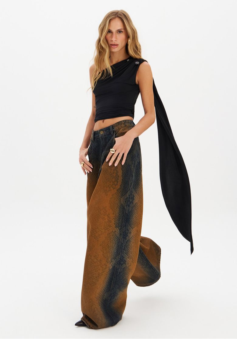Modelo usando blusa ombro único preta com calça ampla estampada.