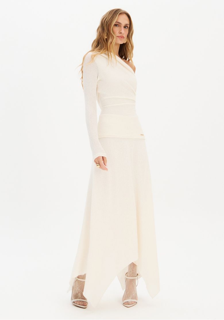 Imagem full body da modelo usando blusa ombro único branca com saia longa de barra assimétrica, vista frontal