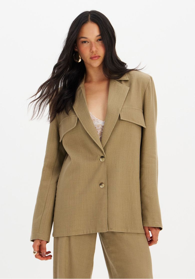 Close do detalhe da lapela clássica, bolso com aba e botão frontal do blazer verde em linho-modal