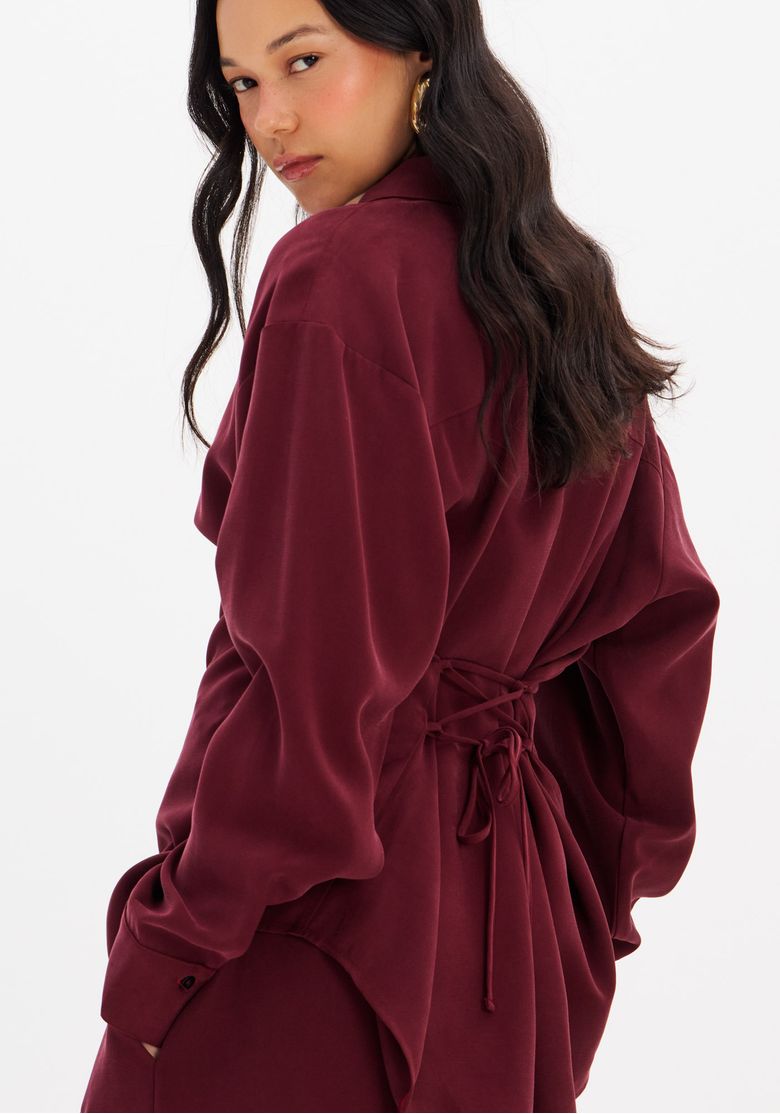 Modelo em look completo com camisa bordô e calça combinando, em ambiente interno.