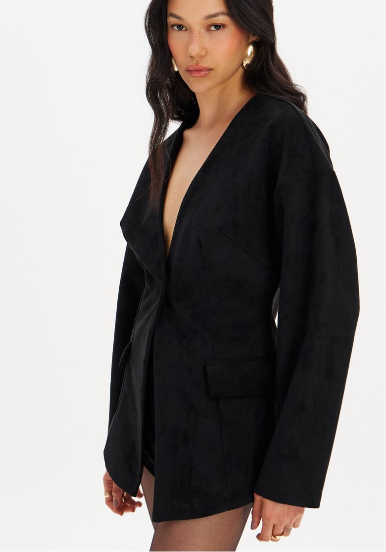 Close frontal do blazer ajustado de suede preto sem gola, evidenciando o decote em V, a posição do botão e o acabamento aveludado do tecido