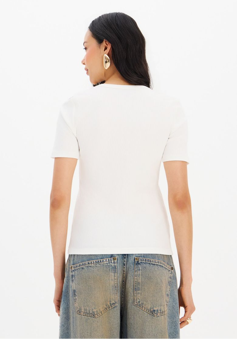 Modelo de perfil usando a blusa canelada branca com acessórios dourados.