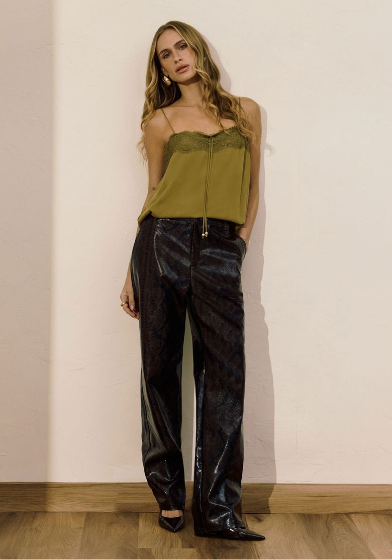Modelo em pose casual, vestindo calça reta de PU com estampa snake marrom e top verde oliva, destacando atitude e caimento longo.