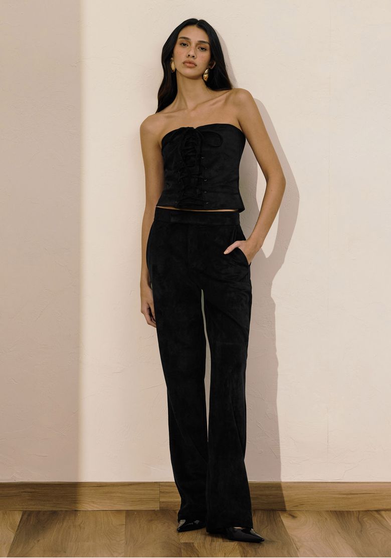 Modelo em ambiente usando calça reta de suede preta cintura média e top bustier, visual full body e bolso faca