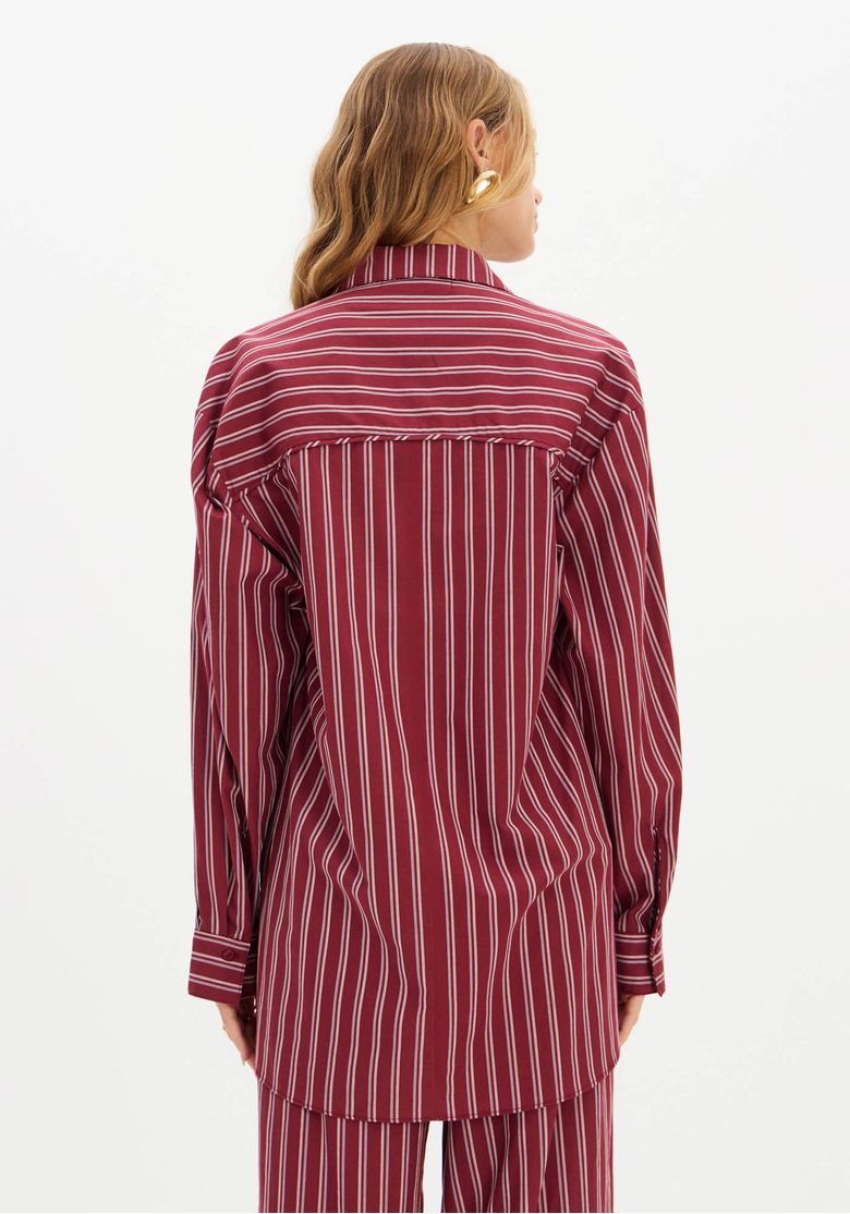 Close-up do tecido listrado em vermelho e branco da camisa oversized.