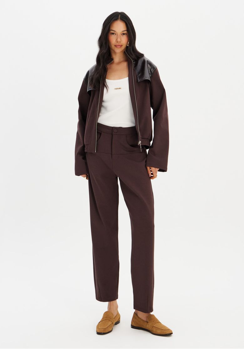 Modelo vestindo calça baggy marrom com jaqueta e top branco.
