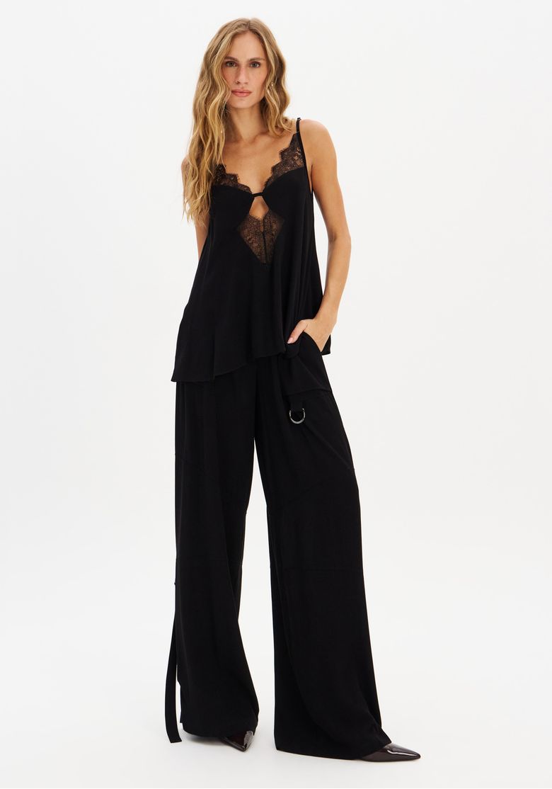 Modelo em estúdio usando calça wide leg preta e top de renda preto, mostrando caimento amplo e bolso lateral com detalhe metálico