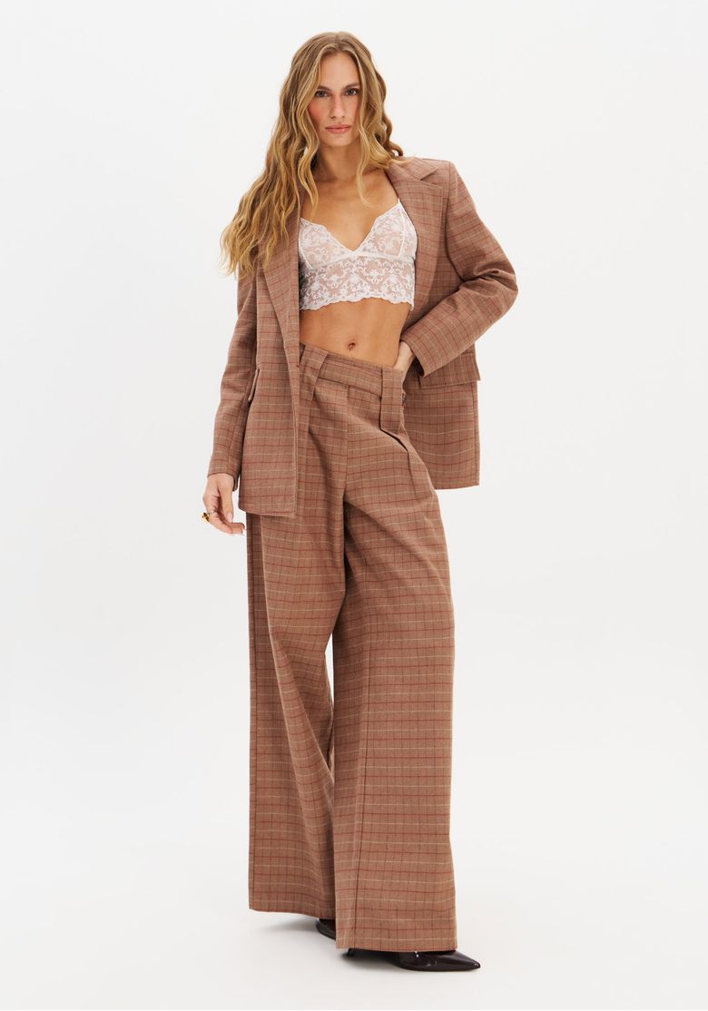 Modelo vestindo calça wide leg xadrez marrom com blazer combinando.