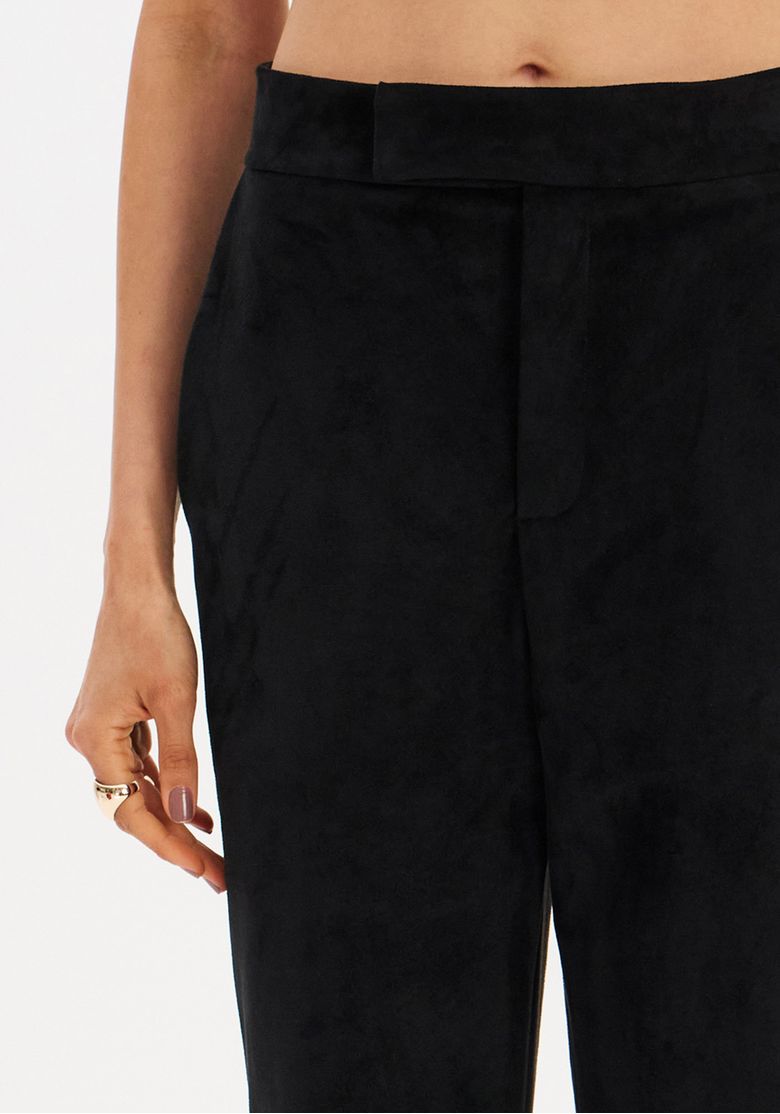 Close do cós e bolso faca da calça reta de suede preta, detalhe do acabamento e fechamento frontal discreto