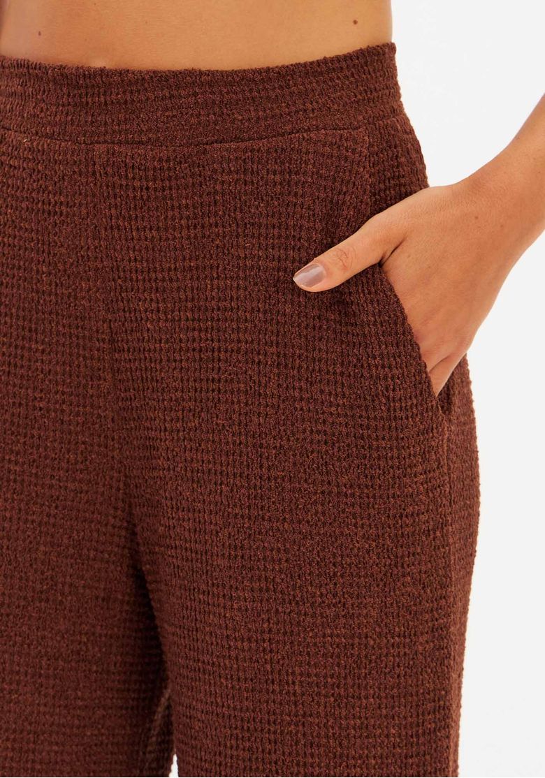 Vista traseira da calça full length em malha texturizada marrom, vestida por modelo, evidenciando cós e acabamento reto das pernas.