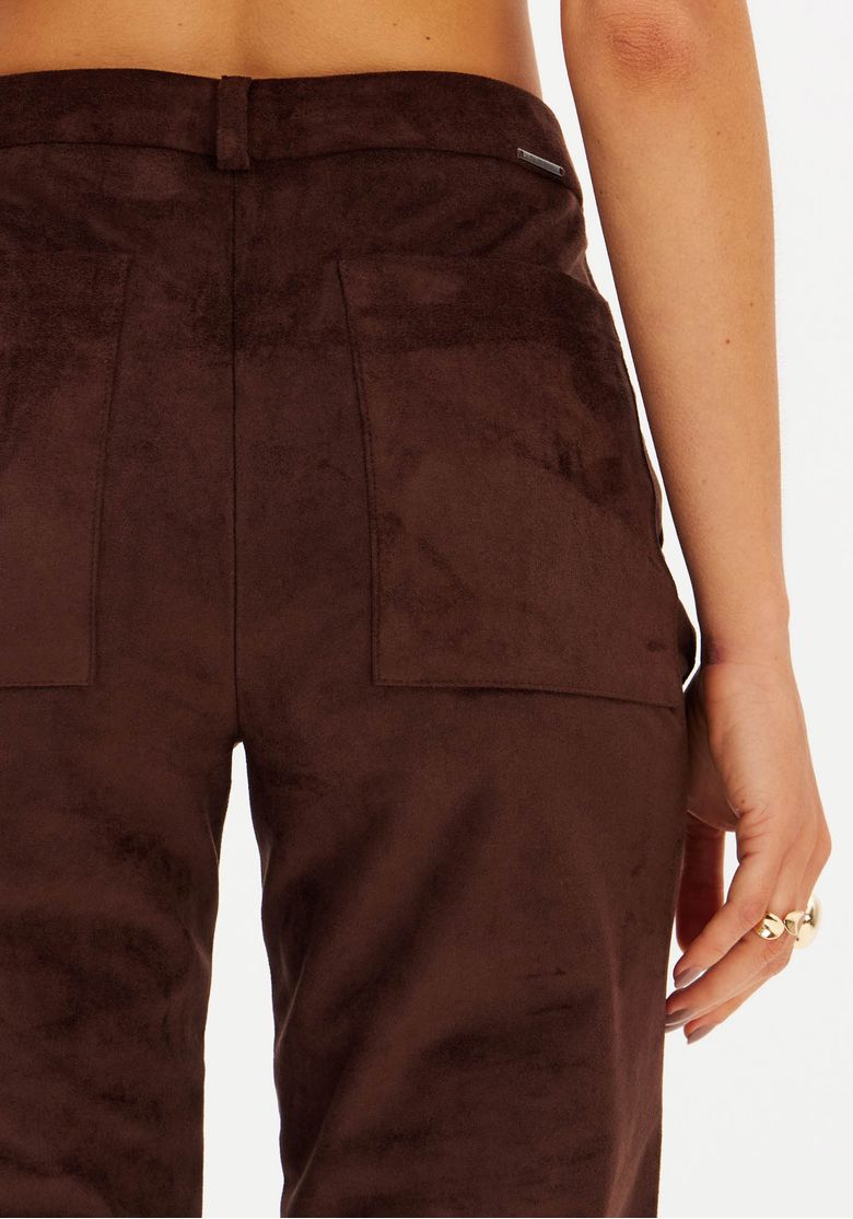 Close-up dos bolsos traseiros chapados da calça skinny em suede marrom.