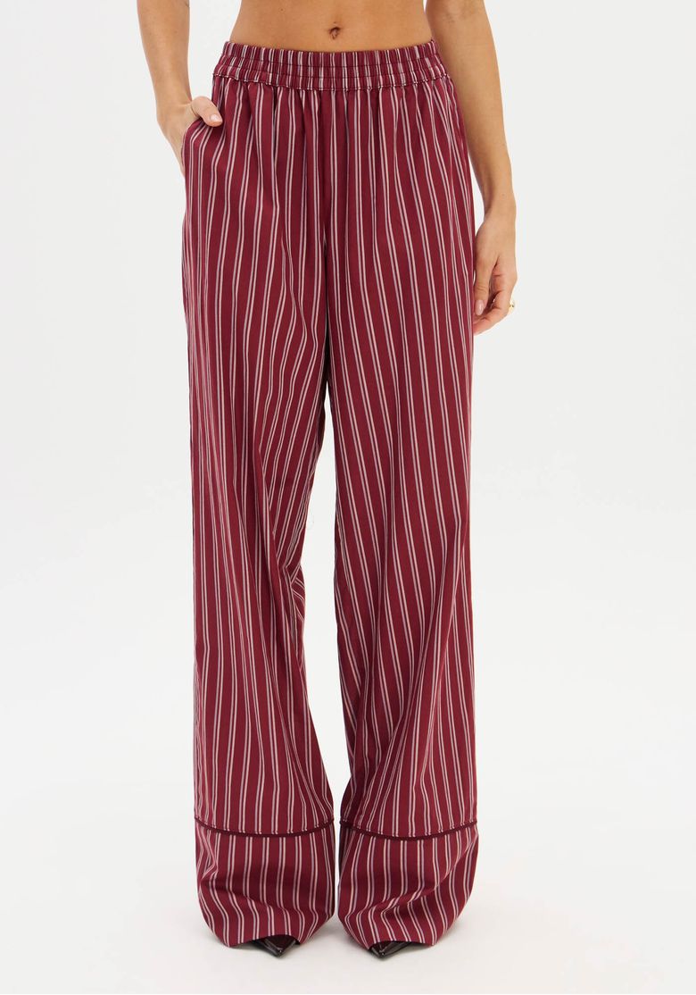 Modelo em estúdio com calça listrada vermelha e blazer bege, vista frontal que destaca a barra larga e o caimento fluido da peça