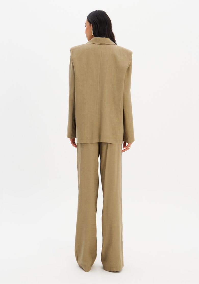 Vista traseira da modelo usando blazer e calça full length verde, silhueta alongada e caimento elegante