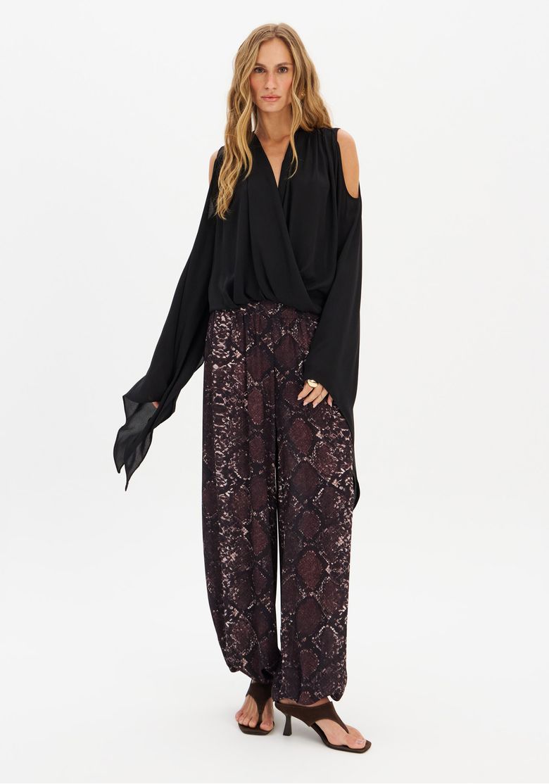 Imagem frontal de modelo vestindo uma blusa preta de mangas longas e calça Aladim estampada com estampa croco marrom, complementada com sandálias de tiras.