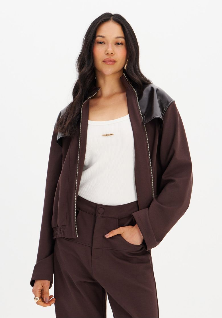 Modelo usando jaqueta bomber marrom aberta com regata branca e calça marrom, destaque para recortes em PU nos ombros e visual casual urbano
