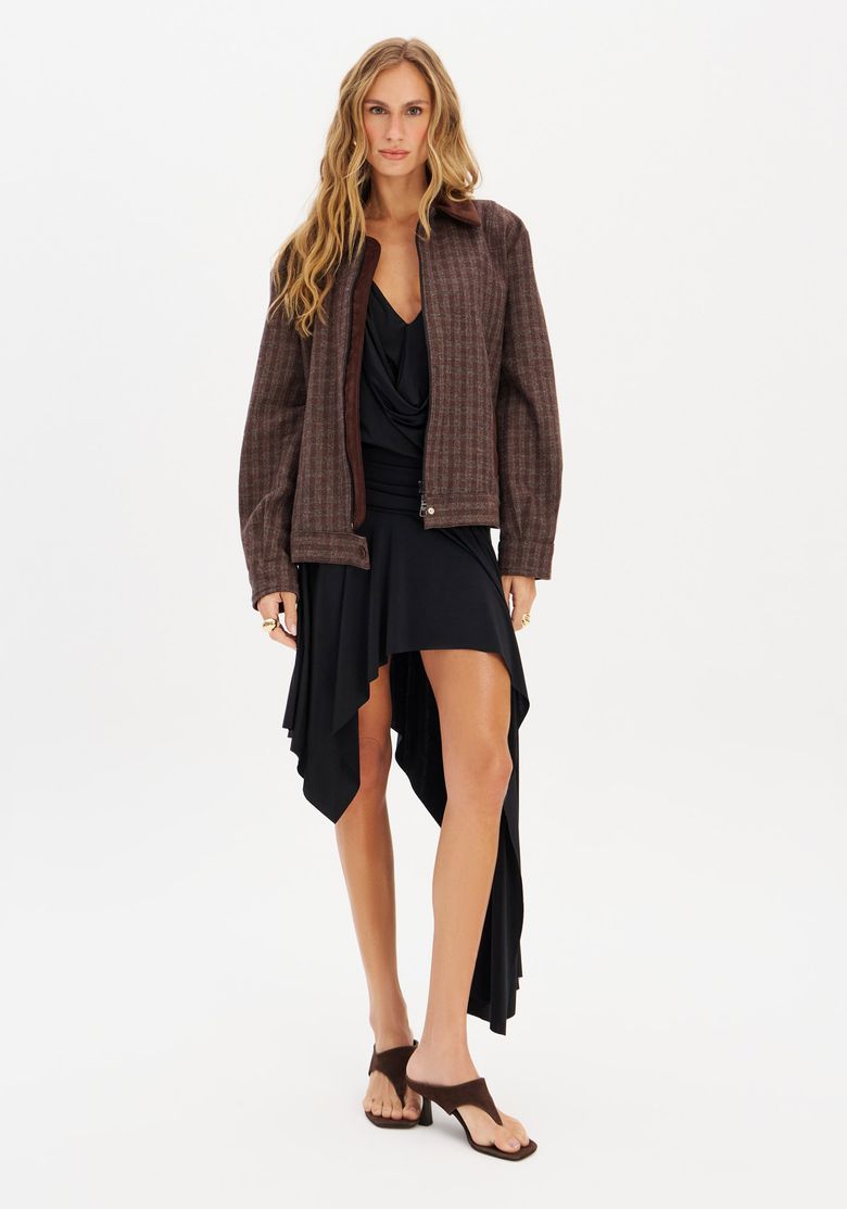 Modelo usando jaqueta bomber xadrez com vestido preto assimétrico.