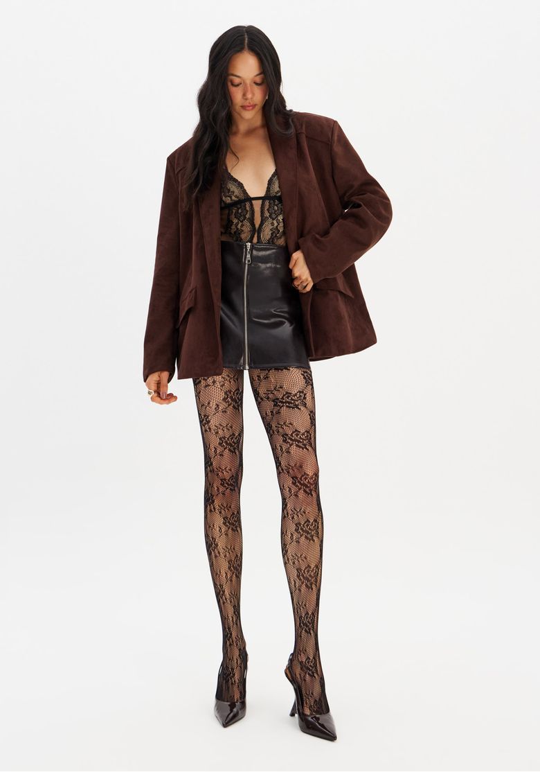 Modelo vestindo saia curta reta em PU marrom com zíper frontal, body de renda preta e blazer oversized — combinação ideal para eventos noturnos.