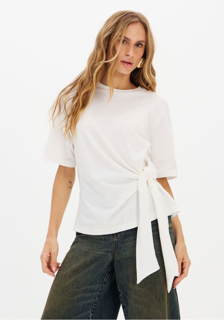 T-shirt branca com amarração na cintura, vista frontal com modelo usando calça jeans.