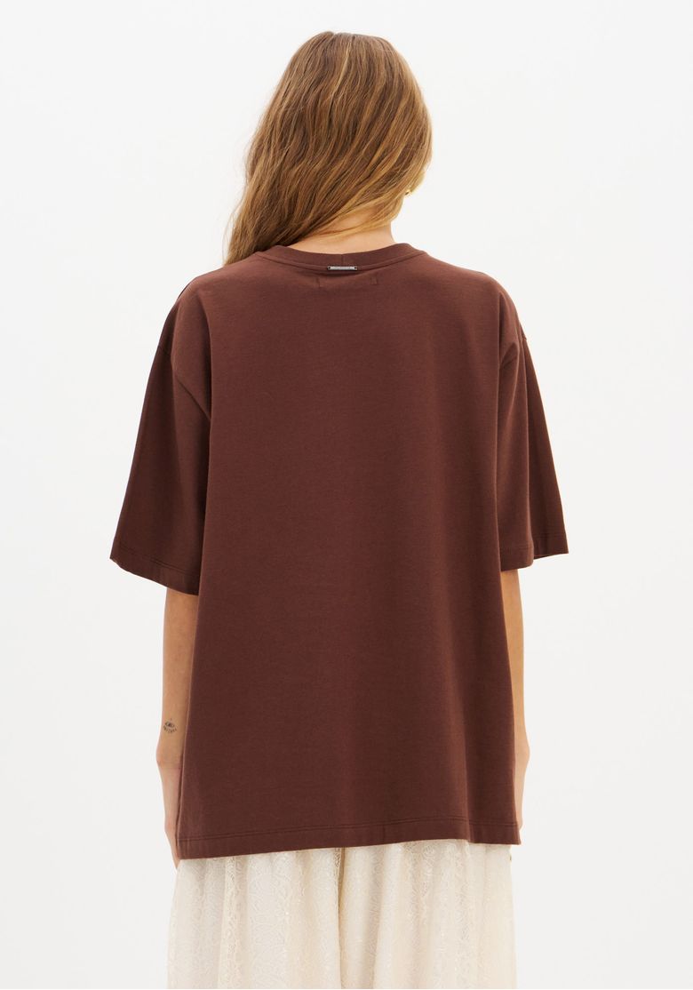 Vista traseira da camiseta oversized marrom exibindo corte reto das costas, acabamento da gola e comprimento alongado da peça.