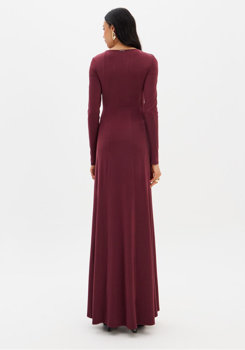 Modelo em parede interna usando vestido bordô super midi, close de frente destacando decote reto e mangas longas
