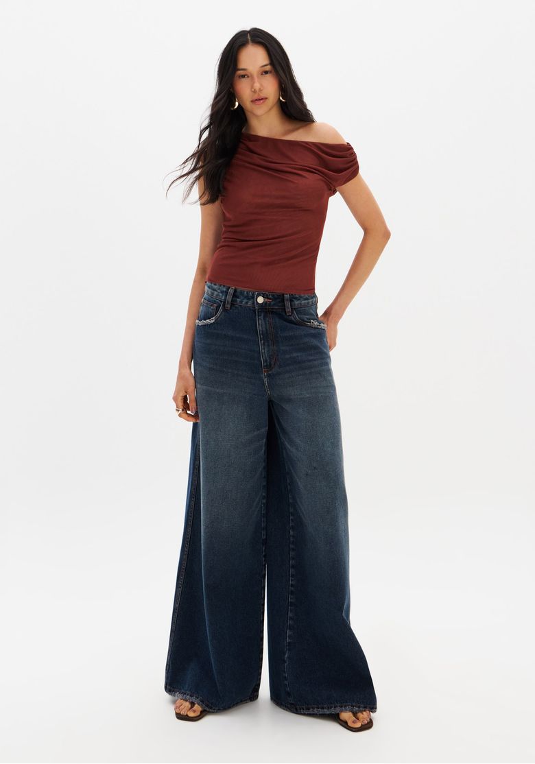 Modelo vestindo calça jeans palazzo azul com pernas amplas e barra desfiada, combinada com top ajustado.