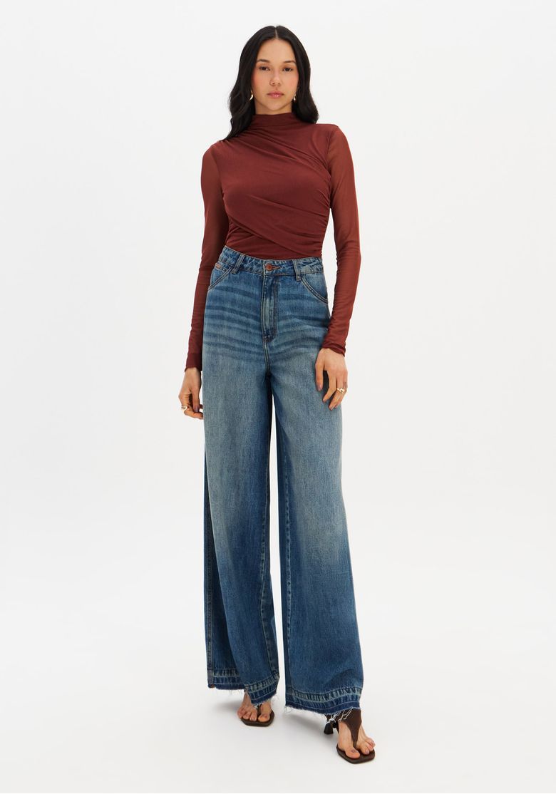 Modelo frontal usando calça jeans relaxed cintura média em denim azul lavagem clássica, look completo com blusa de manga longa