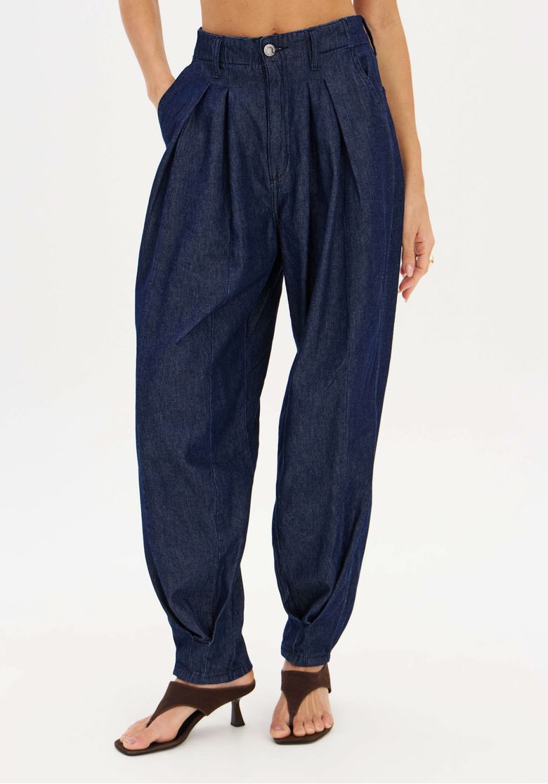 Detalhe frontal da calça jeans slouchy com pregas frontais, bolsos laterais inclinados, cós com passantes e fechamento por botão, lavagem escura