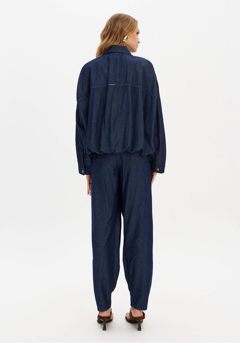 Vista traseira da modelo com jaqueta denim e calça jeans slouchy mostrando caimento longo e barra afunilada