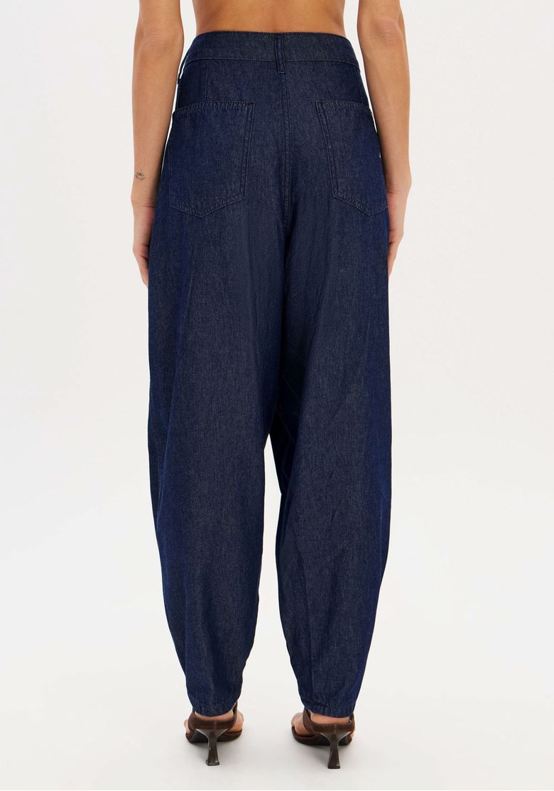 Close das costas da calça jeans slouchy em lavagem escura com bolsos traseiros chapados, costuras aparentes e barra com punho