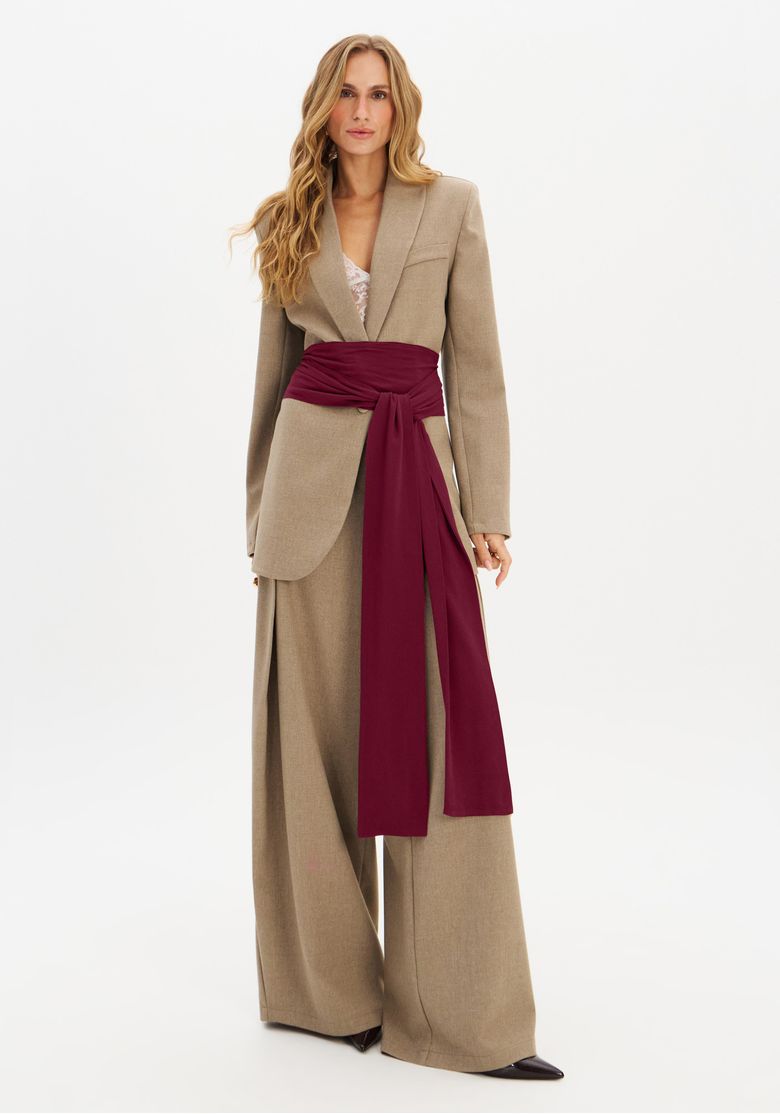 Modelo trajando blazer oversized de alfaiataria em tom neutro com faixa contrastante longa na cintura e calça pantalona, look contemporâneo para escritório