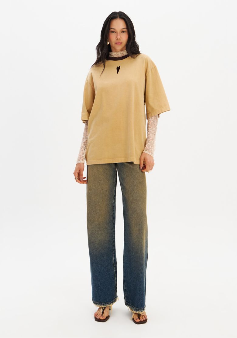 Modelo em corpo inteiro com camiseta oversized bege e calça jeans de perna larga, demonstrando proporção e comprimento da peça.