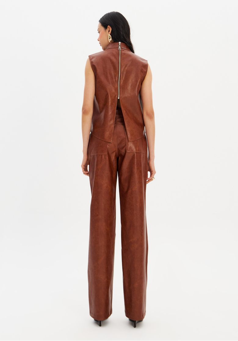 Visão das costas do conjunto em PU marrom com zíper no top e calça reta longa, acabamento que imita couro