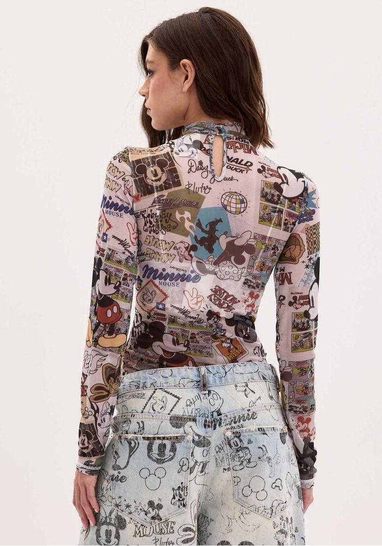 Modelo sentada em cenário de cinema usando a blusa tule estampada por baixo de camiseta branca e calça jeans estampada, look urbano