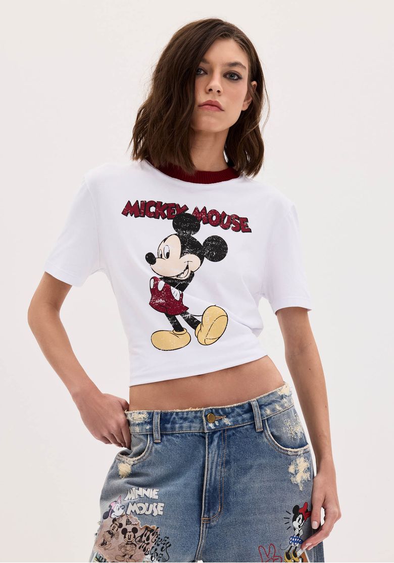 Modelo vestindo camiseta Baby Look Mickey Mouse com estampa frontal e gola contrastante.
