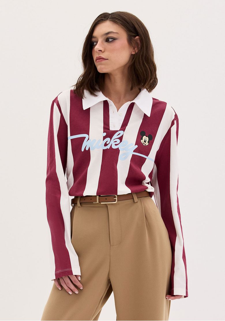 Modelo em estúdio com camiseta listrada manga longa vinho e branco, barra reta e caimento solto combinada com calça caramelo.