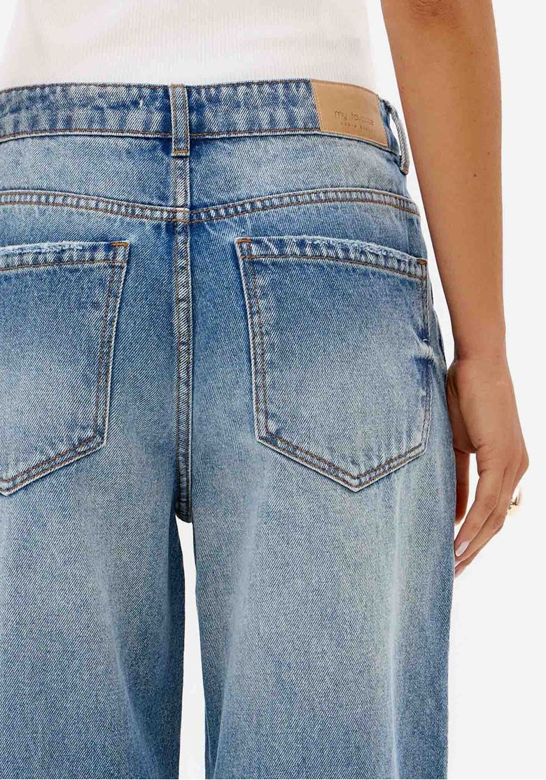 Close traseiro de calça jeans feminina azul clara com bolsos traseiros, cós com passantes e detalhe de lavagem denim