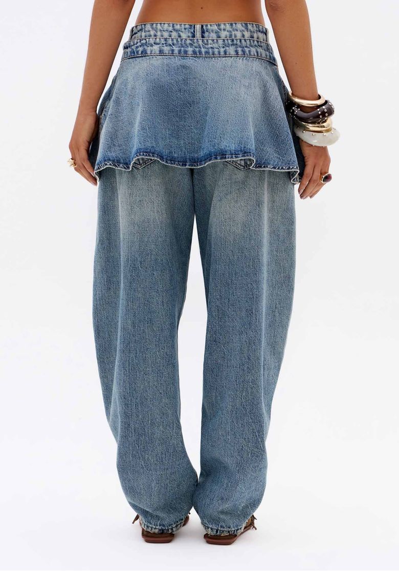 Vista traseira de calça jeans carrot azul feminina com saia sobreposta removível e caimento solto em denim